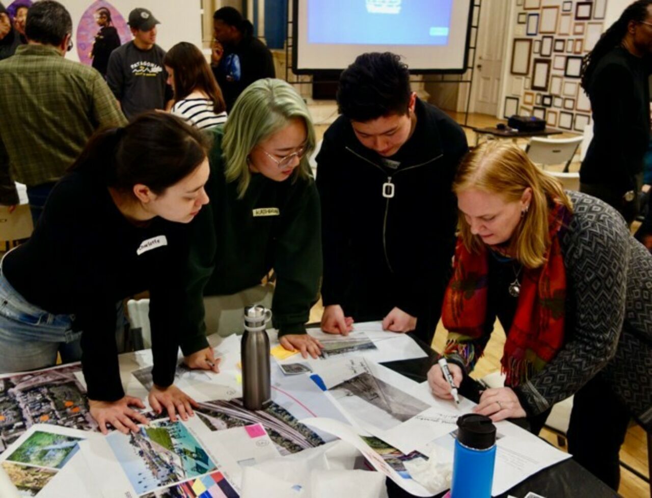 Landscape architecture students and community members looking at designs spread across table at a Community charette in Hazelwood, PA.