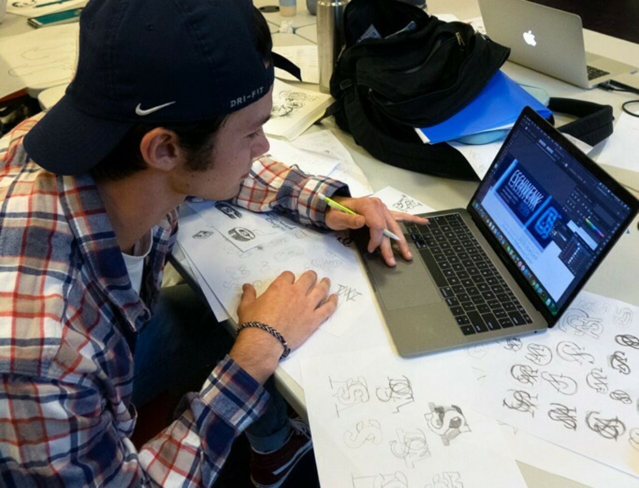 Graphic design student in class working on a logo through various drawings on paper and refiningn on his computer.