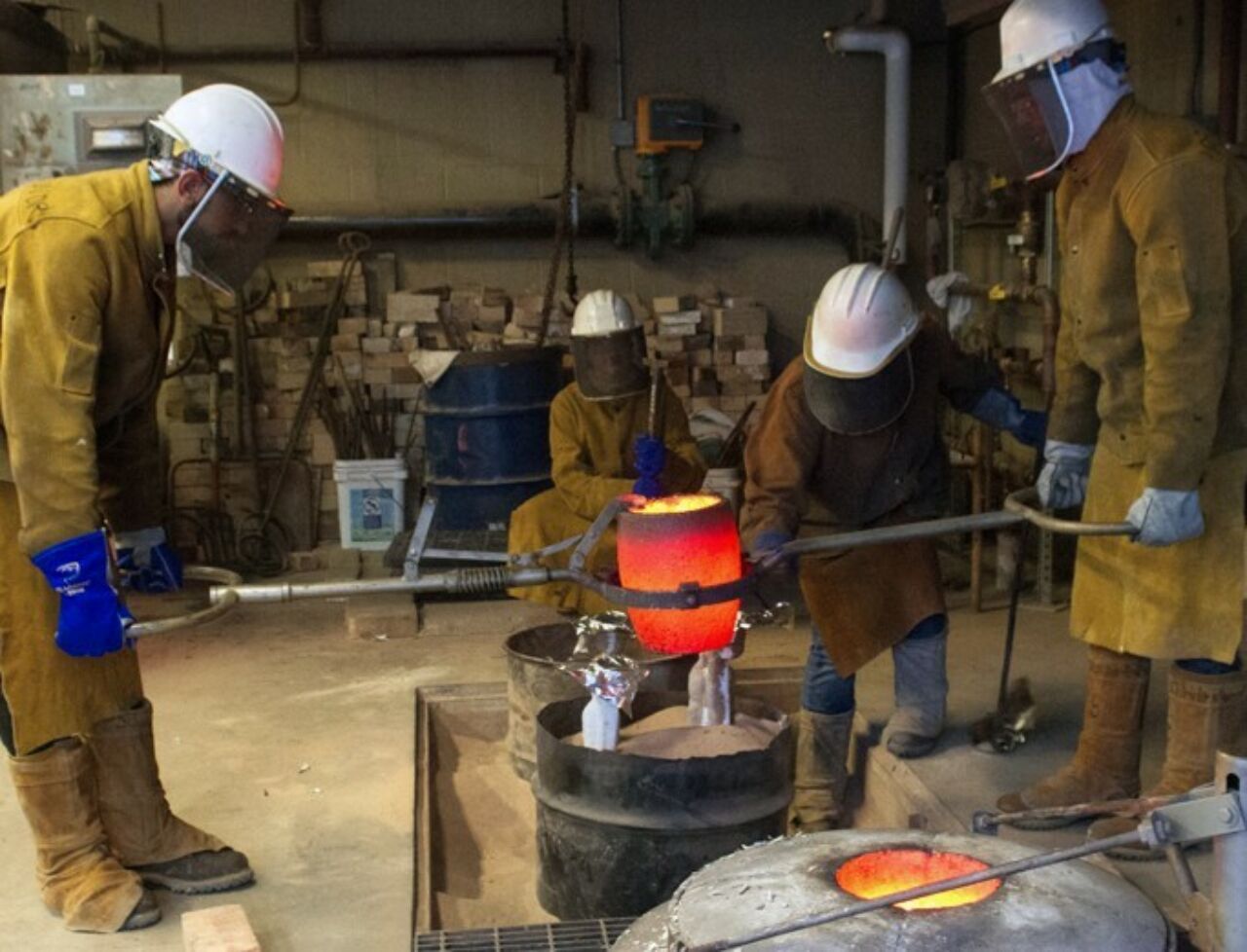 SoVA students in protective clothing and headgear pouring metal into a mold.