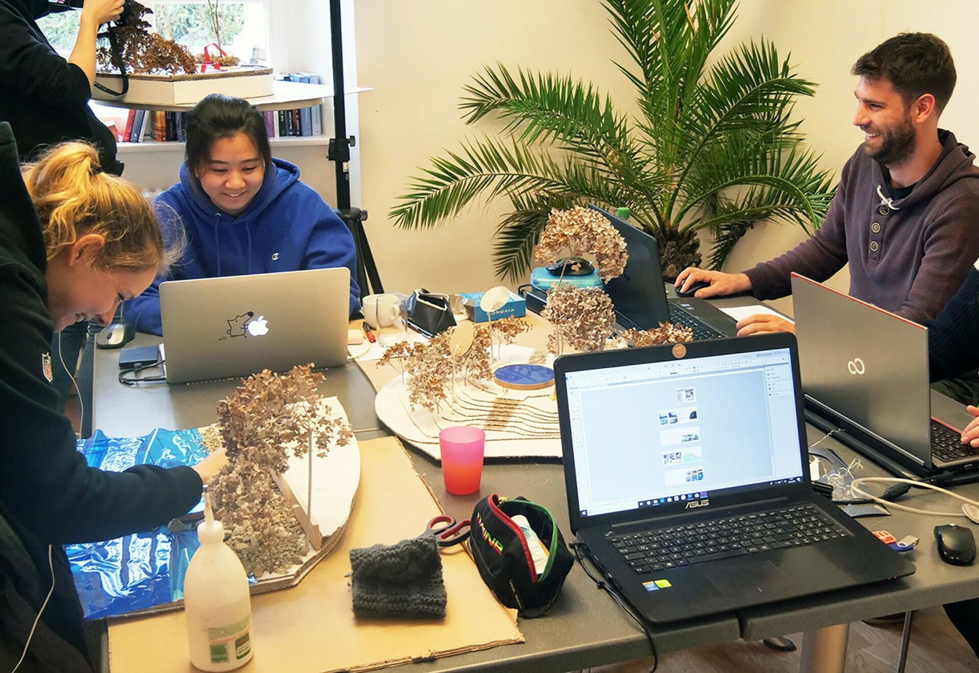 Two students sitting and one student standing around a table working on designing a landscape architecture model.