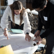 Two students reviewing architectural drawings on a table.