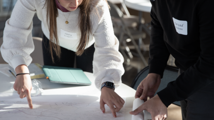 Two students reviewing architectural drawings on a table.