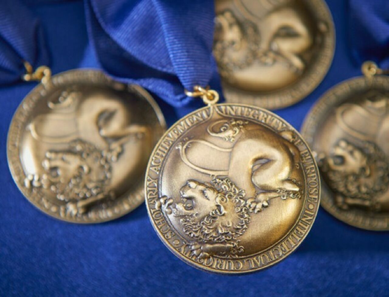 Close-up shot of four Schreyer Honors College medals on a rich blue background. Photo by Steve Tressler.