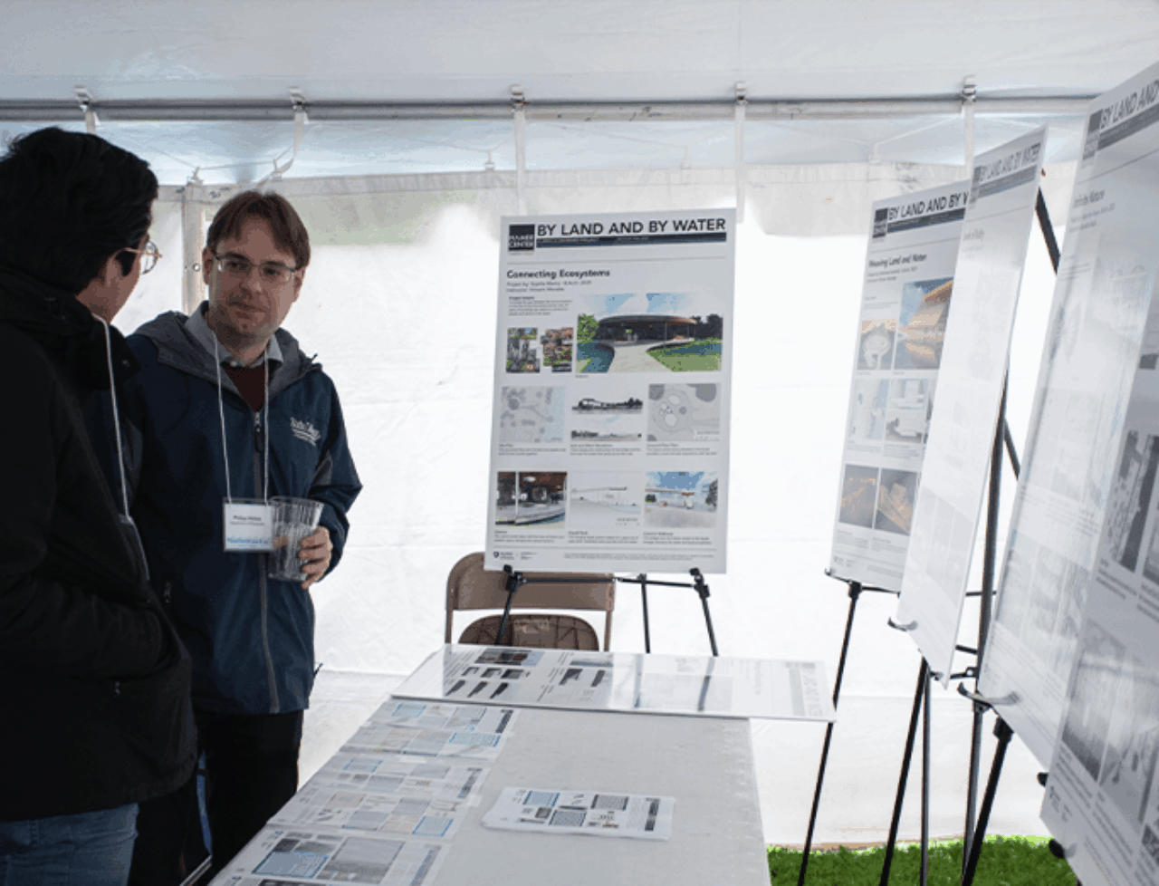 Two communities members talk in front of Hamer Center posters at Floodfest.