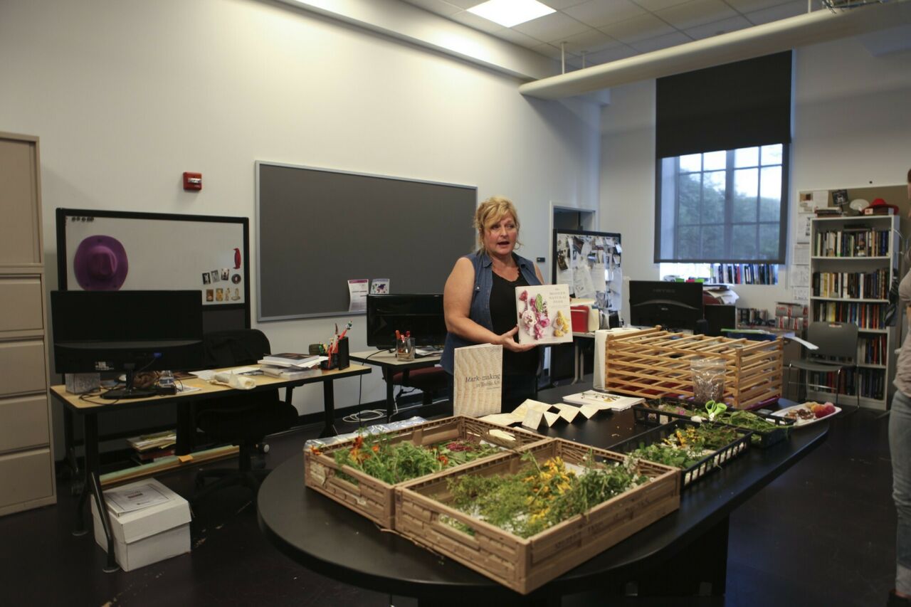 An instructor holding up a book in front of a table with an assortment of dried flowers in crates.