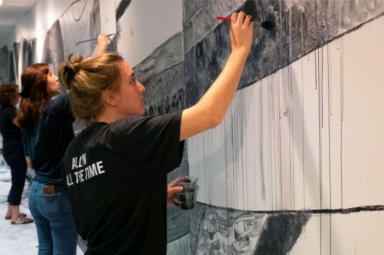 Three students painting together on a long wall project in the Woskob Gallery