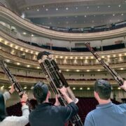 Three students hold up bassoons toward audience in auditorium, with backs to camera.