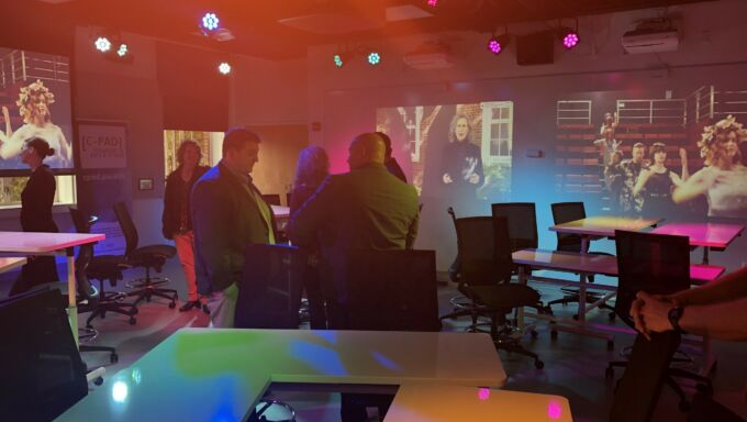 white tables and black desk chairs, people in business wear talking under colorful lights