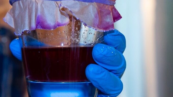 Red dye in clear glass held by blue gloved hand