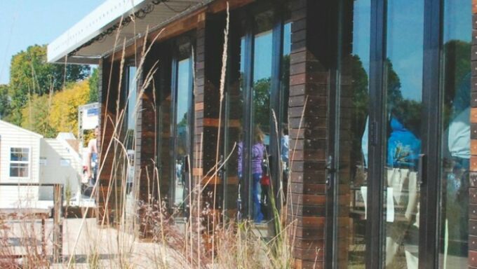 Cropped view with an energy-efficient house and wild grasses in the foreground, with a group of students and the Washington Monument in the background.