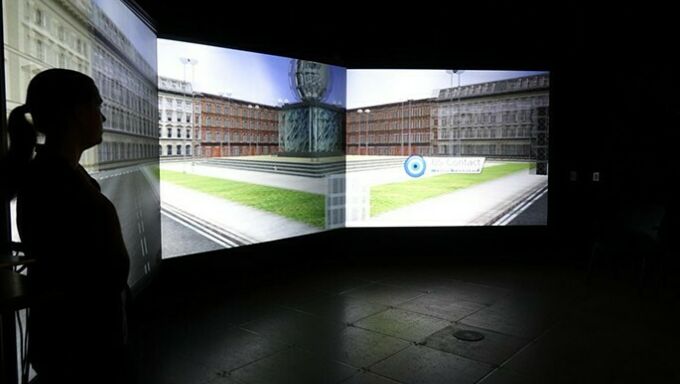 A female student's profile at left against an immersive reality background on a screen behind her in a darkened lab.