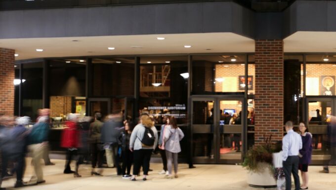 People standing and moving in front of the illuminated entrance to Eisenhower Auditorium