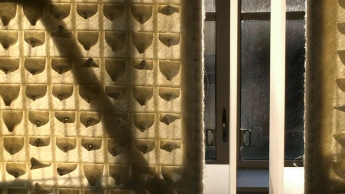 Panels of textured felt hanging in front of a glass window.