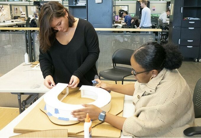 Two female architecture students work on building an architectural model out of cardboard