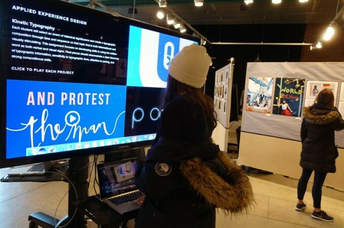 Undergraduate graphic design student work exhibition: showcasing a student watching a large video display of bright colored graphics.