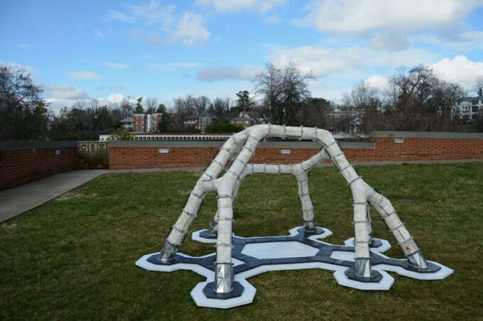 A white architectural structure with six legs on a patch of grass.