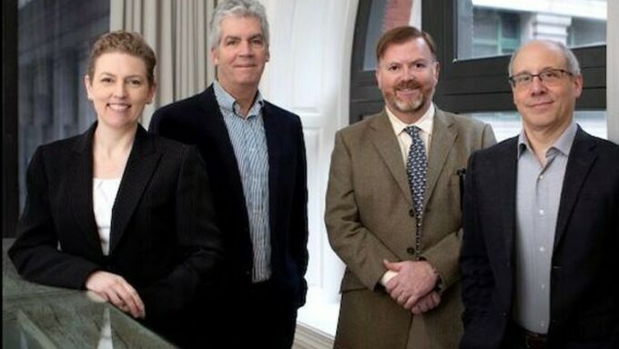 Three men and a woman in business attire smile at the camera.