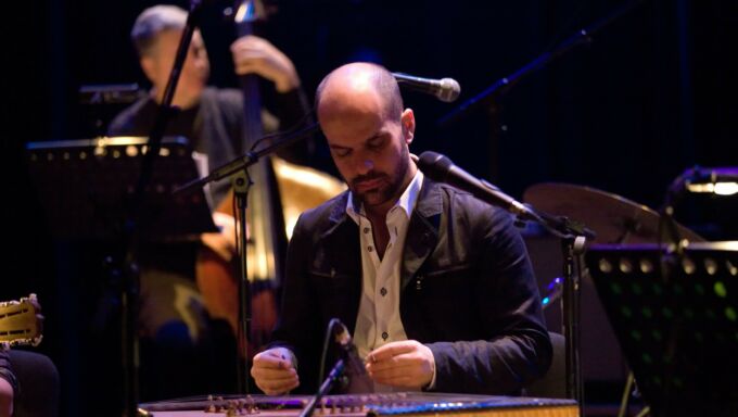 A man sits at and plays a santur, a Middle Eastern-style of hammered dulcimer.