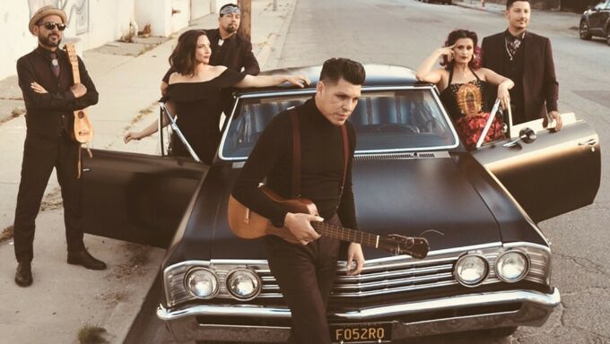 A group of men and women dressed monochromatically stand glamourously around a souped up hot rod.