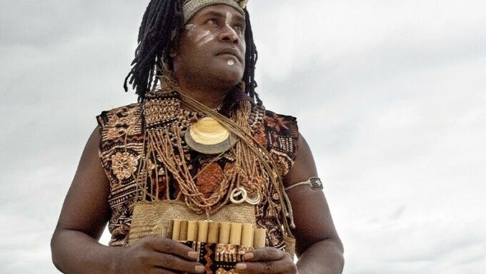 A man wearing a coastal headdress looks off into the distance.