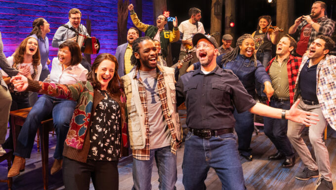 A diverse group of people stand in a cluster and sing and dance together.