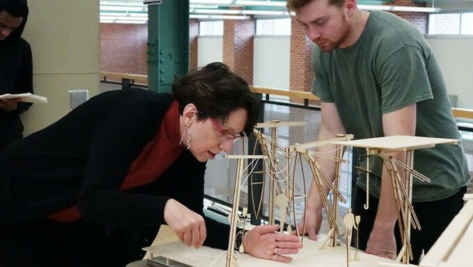 Alexandra Staub, at left, leans over a table while critiquing a student's model while he watches.