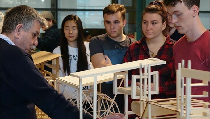 A side profile of Loukas Kalisperis pointing at a model on a desk in front of him while students watch.