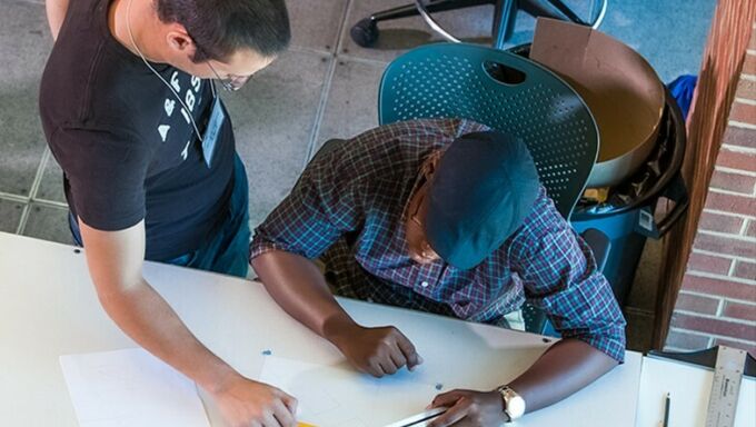 A faculty member instructs an architecture student as he sits at his drawing table.