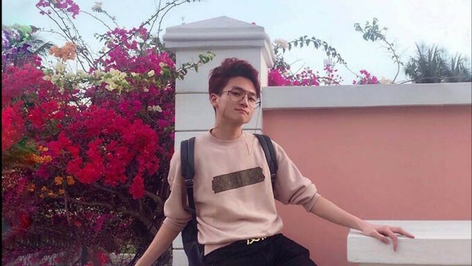 Yiwei Leo Wang posing for a photograph in front of a pink wall around flowers.