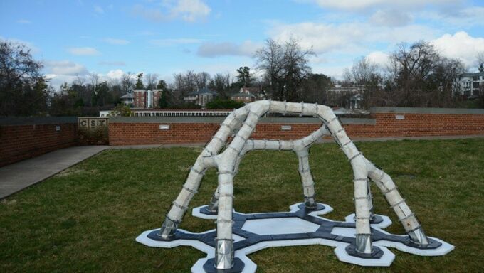 A white architectural structure with six legs on a patch of grass.