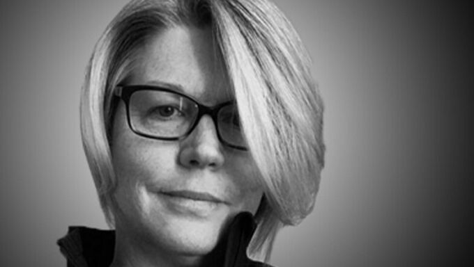 Black and white head shot of a woman with grey short hair and black-rimmed glasses