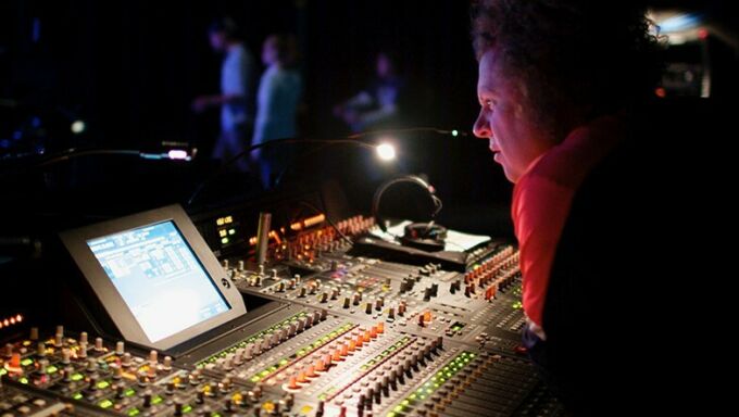 Man in red shirt leaning over a soundboard during a live performance