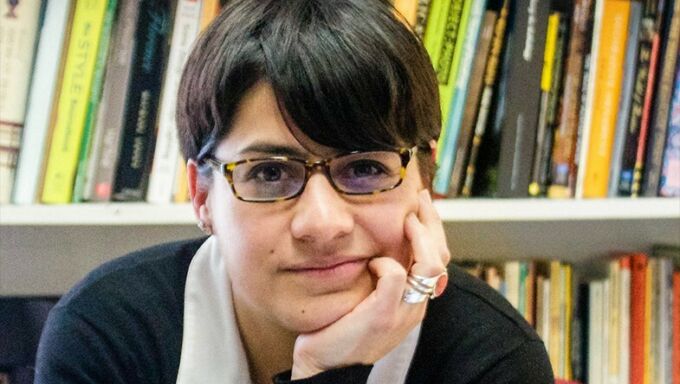 Woman with short, dark hair and dark-rimmed glasses resting her head on her hand