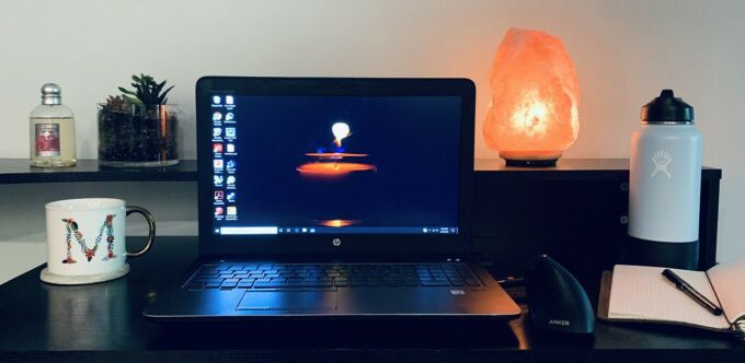 A home work station with a loptop, water bottle, Himalayan salt rock lamp, plant, coffee mug, and stechpad with a pen.