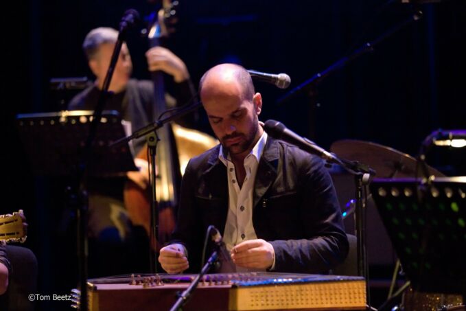 A man sits at and plays a santur, a Middle Eastern-style of hammered dulcimer.