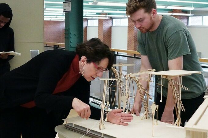 Alexandra Staub, at left, leans over a table while critiquing a student's model while he watches.