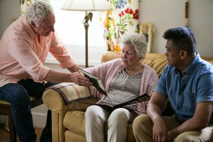 An elderly man showing a framed photograph to an elderly woman