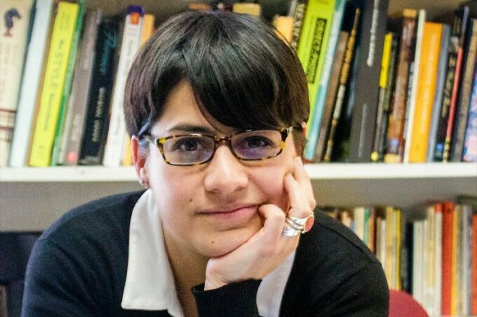 Woman with short, dark hair and dark-rimmed glasses resting her head on her hand