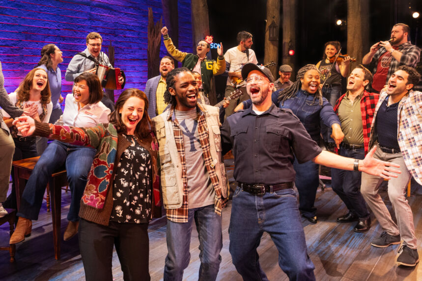 A diverse group of people stand in a cluster and sing and dance together.