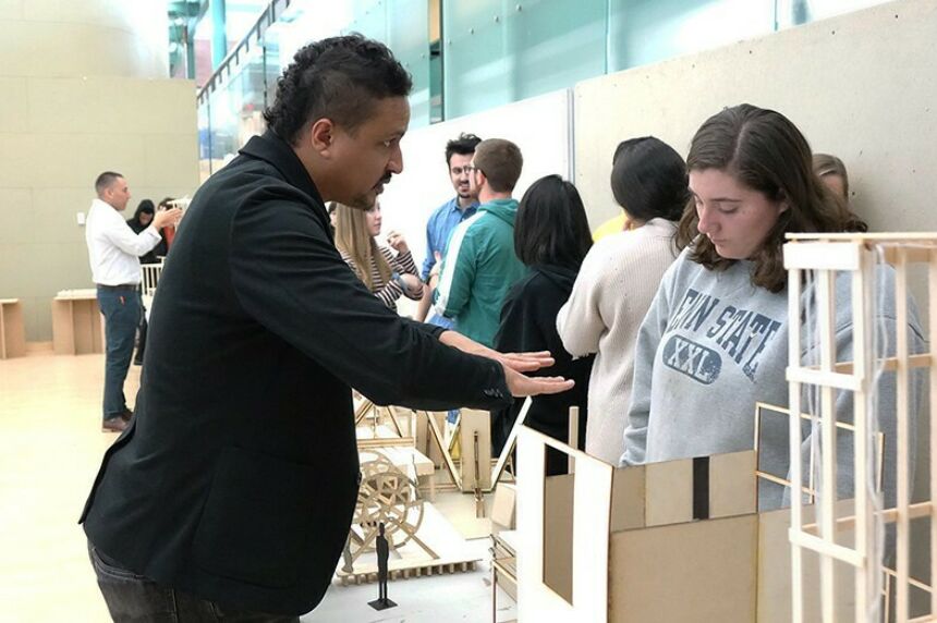 DK Osseo-Asare stands at left while talking with a female student in front of him and her model in between them on a table during a review.