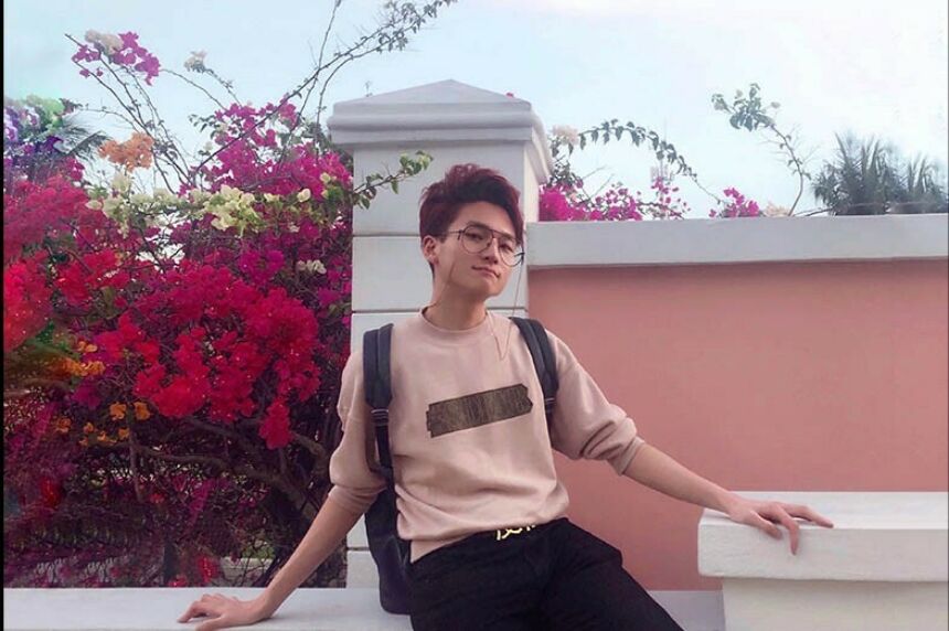 Yiwei Leo Wang posing for a photograph in front of a pink wall around flowers.