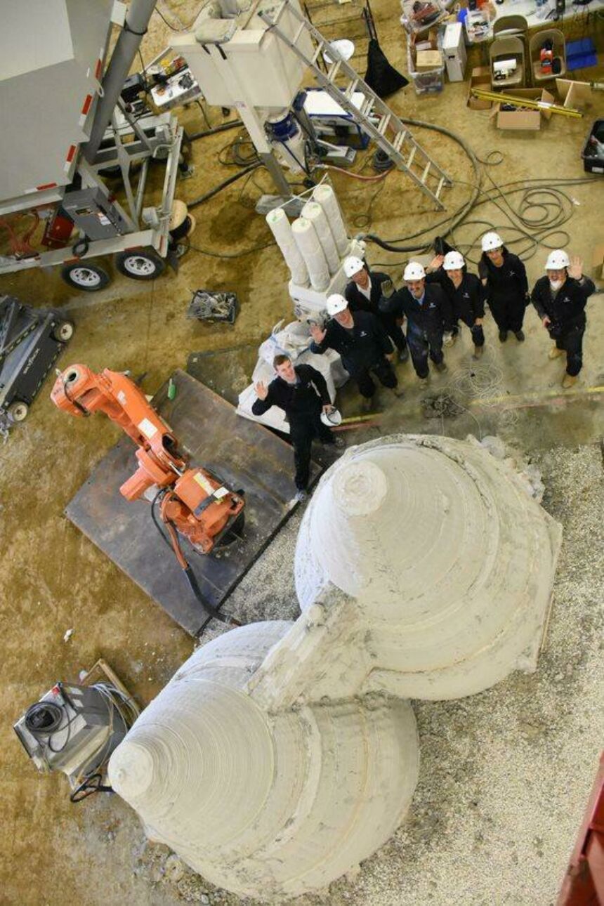 Overhead view of Penn State Mars team standing by orange robotic arm and full-size 3d fabricated concrete dwellings