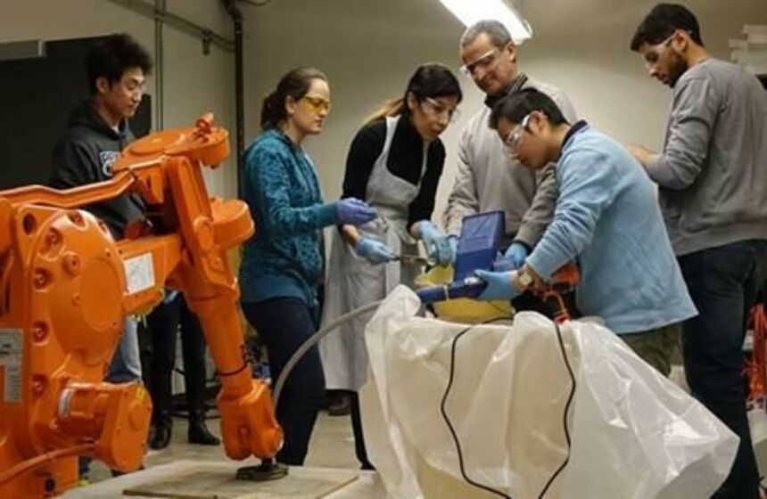 Students and advisers gathered around industrial robot arm performing concrete test prints