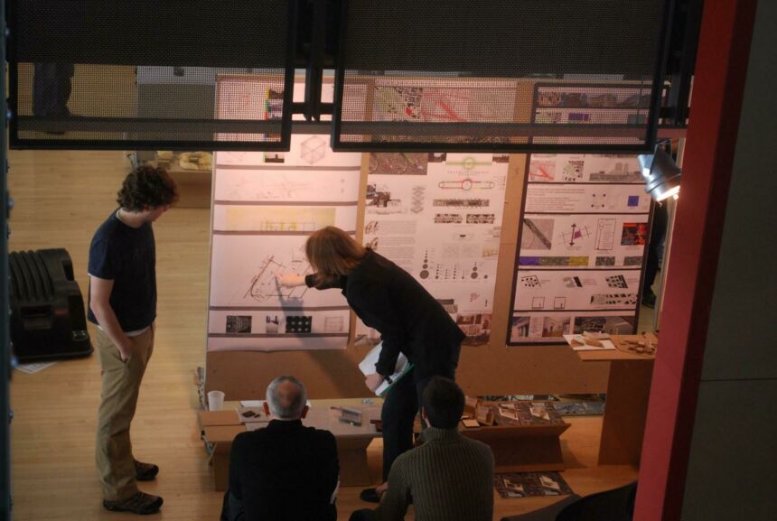 Overhead photo of Ute leaning forward as she points to an area on an architectural diagram posted on a board while talking to her third-year students.